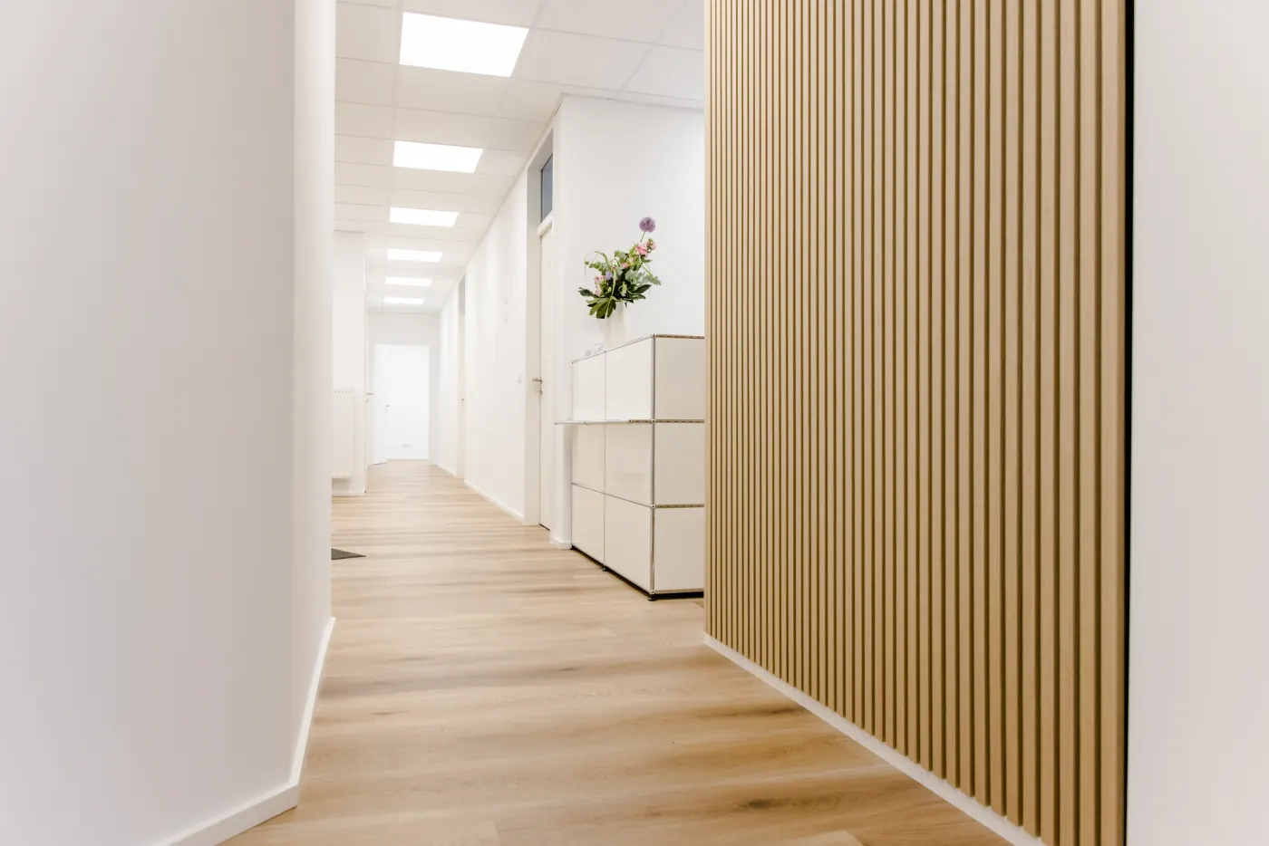 Heller Praxisflur mit Holzlamellenwand und Zugang zu den Behandlungsräumen