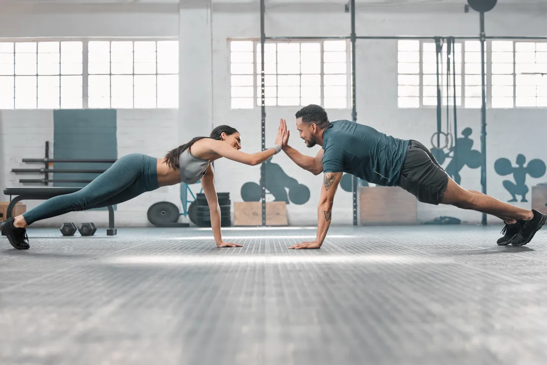 Zwei Trainierende klatschen sich in der Liegestützposition im Fitnessstudio ab